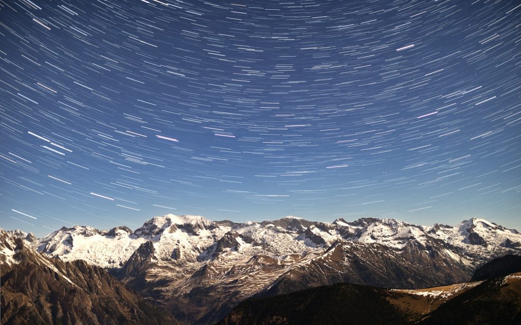 A view of a mountain range with a star trail in the sky
